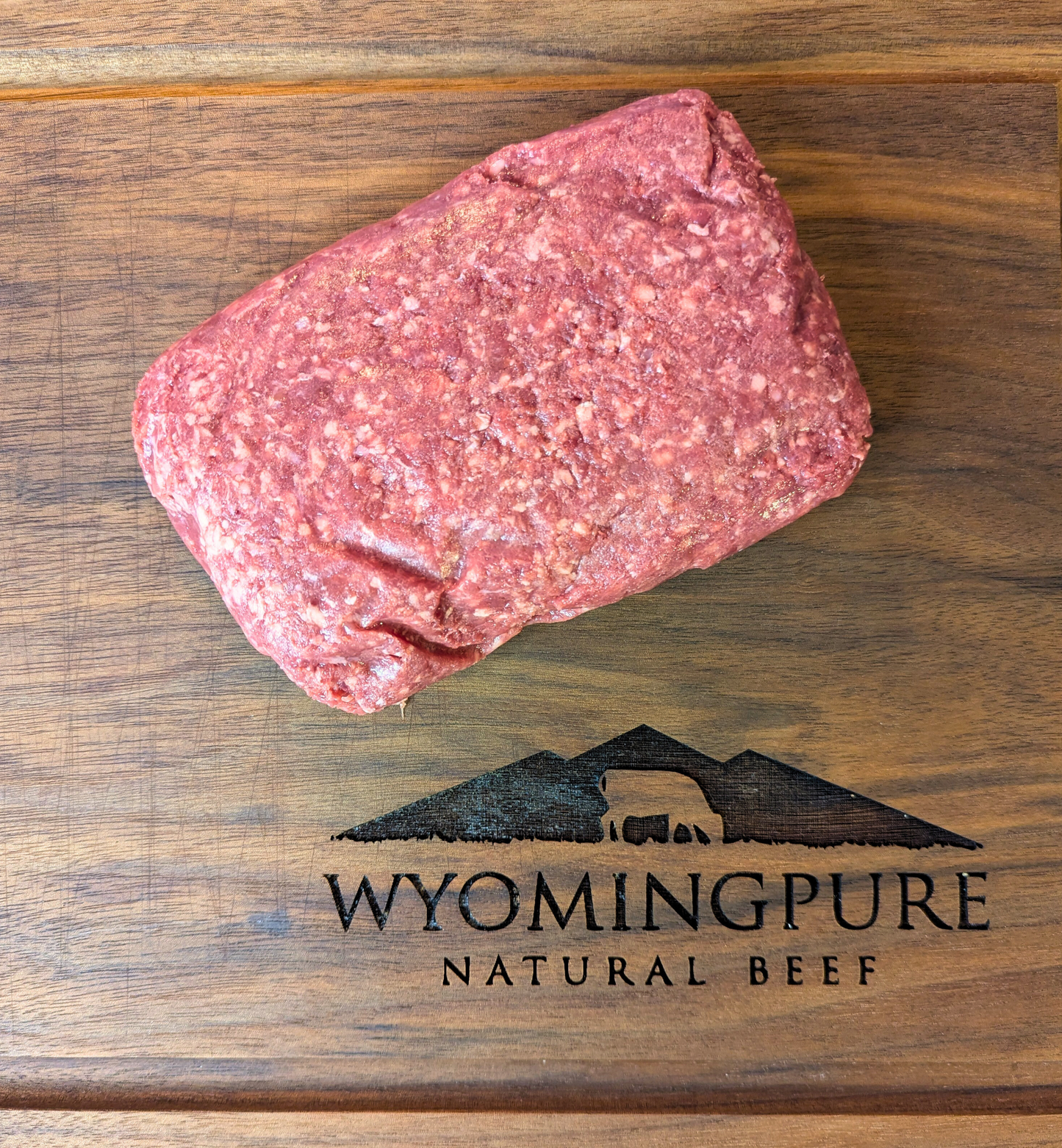 Raw ancestral ground beef with organ meat on a wooden cutting board with Wyoming Pure Natural Beef logo.