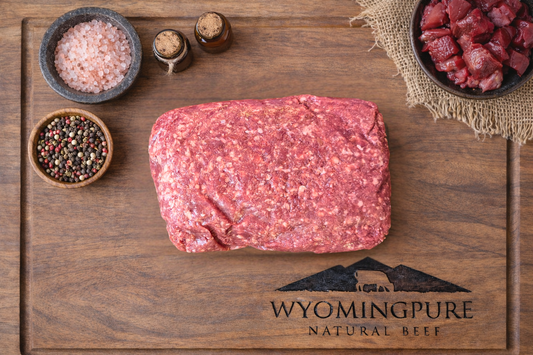 Raw ancestral ground beef with organ meat on a wooden cutting board with Wyoming Pure branding, surrounded by spices and a small bowl of organ meat
