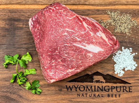 Raw arm roast beef on a wooden board with herbs and spices, branded 'Wyoming Pure Natural Beef'.